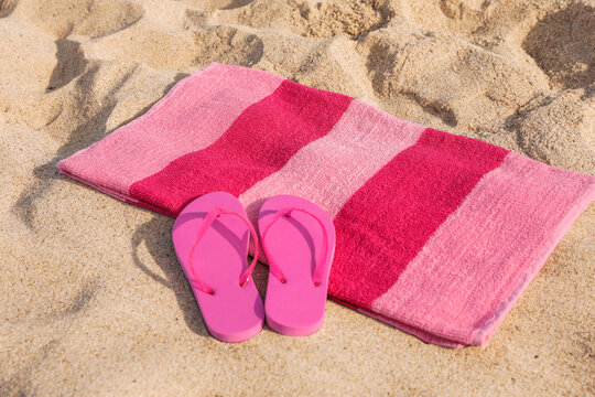 Beach towel and stylish slippers on sand