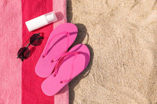 Beach towel with slippers, sunglasses and sunscreen on sand, top view. Space for text