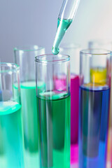 Dripping liquid from pipette into test tube on grey background, closeup