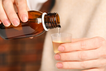 Woman pouring syrup from bottle into measuring cup, closeup. Cold medicine