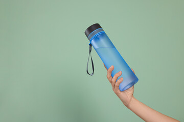 Woman holding bottle of water on green background, closeup. Space for text