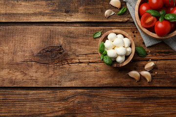 Fototapeta na wymiar Delicious mozzarella balls in bowl, tomatoes and basil leaves on wooden table, flat lay. Space for text