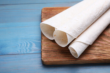 Delicious rolled Armenian lavash on light blue wooden table, space for text