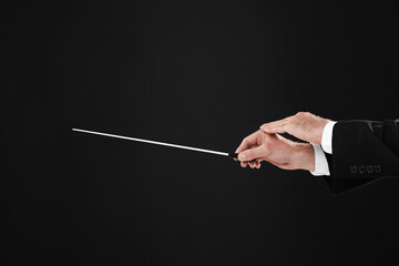Professional conductor with baton on black background, closeup