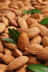Many delicious almonds and fresh leaves as background, closeup