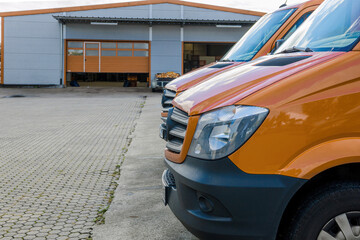 Front part of a row of two orange delivery vans in front of logistics warehouse center - modern transportaiton of goods to customers