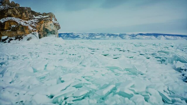 Lake Baikal, flying over ice debris, blue snow hummocks. A ridge of mountains and a yellow rock in the background. Baikal, Siberia, Russia. Drone aerial shot 4k