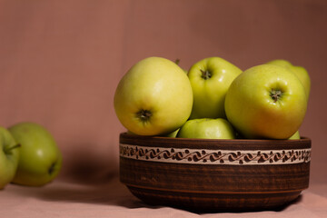 dark clay bowl with a light ornament and green apples - golden on a pink background