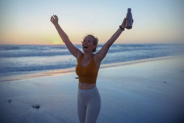 happy fit sports woman rejoicing at beach at sunset