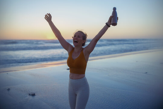 happy fit sports woman rejoicing at beach at sunset