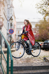 Fototapeta premium woman in red rain coat outdoors on city street riding bicycle