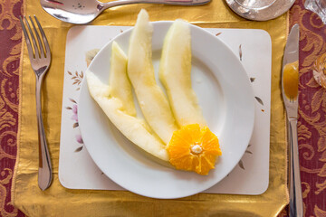 Slices of honeydew melon garnished with a slice of orange served as a starter in a three course meal.