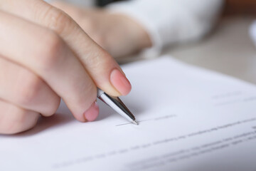 Woman signing document at table in office, closeup