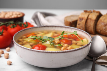 Tasty chickpea soup in bowl and ingredients served on white table, closeup