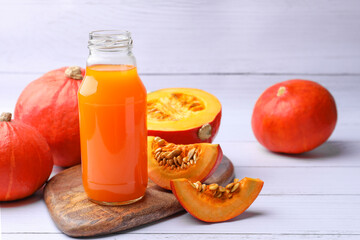 Tasty pumpkin juice in glass bottle and pumpkins on white wooden table. Space for text