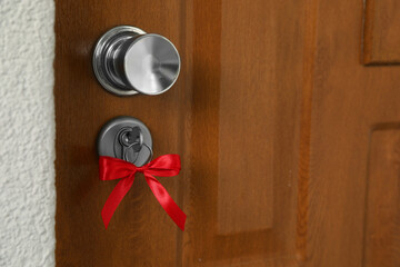Fototapeta premium House key with red bow in door lock, closeup. Housewarming party