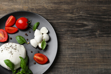 Delicious mozzarella with tomatoes and basil leaves on wooden table, top view. Space for text