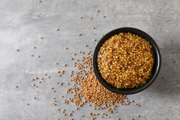Bowl of whole grain mustard and seeds on grey table, top view. Space for text