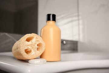 Natural loofah sponge and shower gel bottle on washbasin in bathroom, space for text