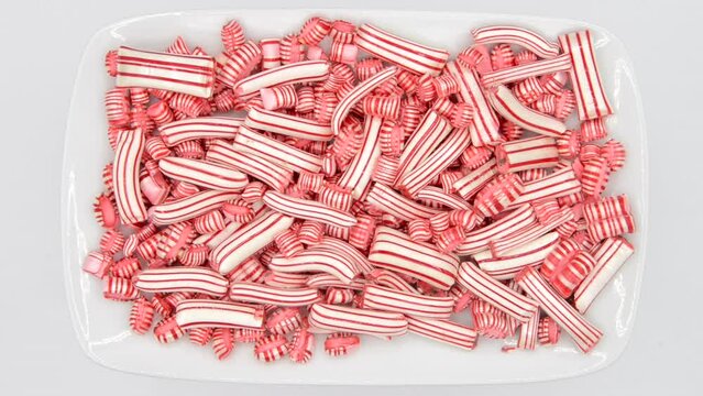 HD video zooming in on rectangular plate of traditional classic red and white peppermint candies on white background.
