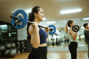 young asian woman lifting barbell in front of chest during exercise in fitness room