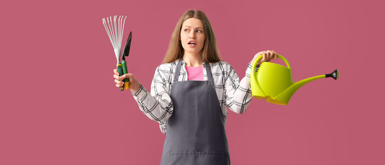 Young woman with watering can and gardening tools on pink background