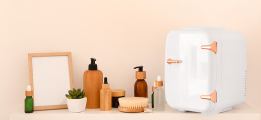 Shelf with small refrigerator and cosmetic products near light wall
