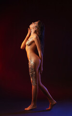 Naked young woman with golden foil on dark background