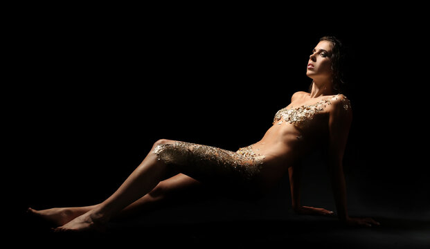 Naked young woman with golden foil lying on black background