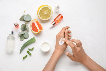 Female hands with natural cream and essential oil on light background