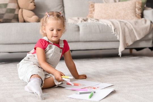Cute little girl with felt-tip pens sitting on floor at home