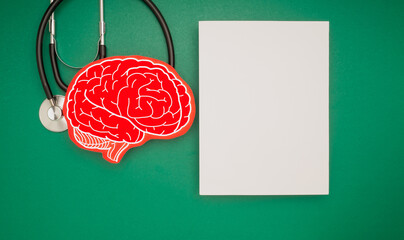 A brain shape symbol and a stethoscope and a blank white paper on a green background