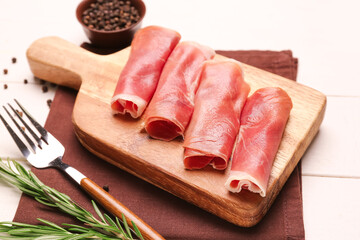 Board with rolled slices of tasty ham on light wooden background