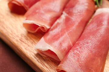 Wooden board with rolled slices of delicious ham, closeup