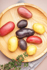 Wooden plate with different raw potatoes and thyme on color background, closeup