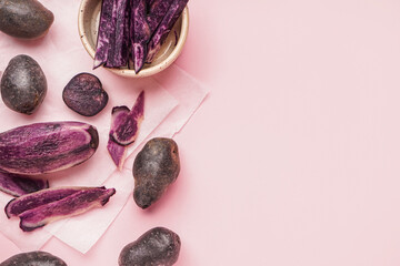 Raw purple potatoes and peel on pink background