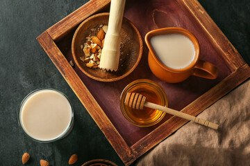 Wooden board with jug of almond milk, honey and nuts on dark background, closeup