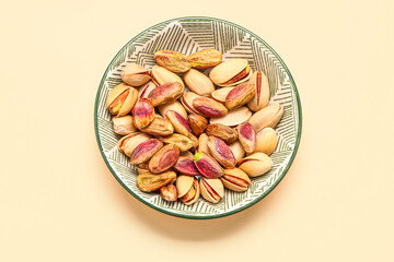 Plate with tasty pistachio nuts on beige background