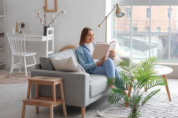 Young woman reading magazine on grey couch at home