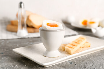 Holder with soft boiled egg and toasted bread on grey table