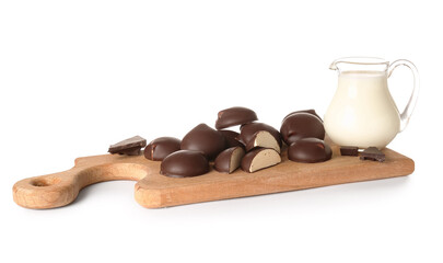 Cutting board with sweet chocolate bird's milk candies and jug of milk on white background