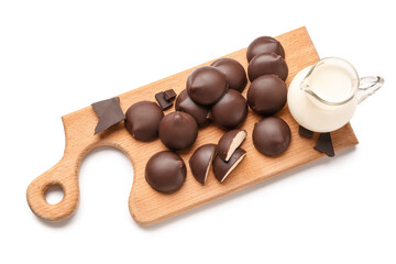 Cutting board with sweet chocolate bird's milk candies and pitcher of milk on white background