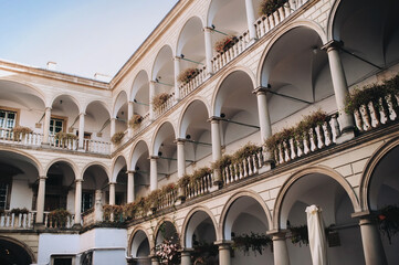 Old eastern european Renaissance three-story arcade, roses and other flowers in hanging pots on the balconies. Ancient architecture of Lviv, Ukraine. View of the patio from below. © shchus