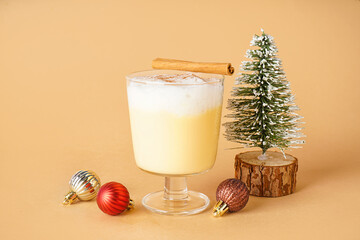 Glass of tasty eggnog cocktail and Christmas decorations on color background