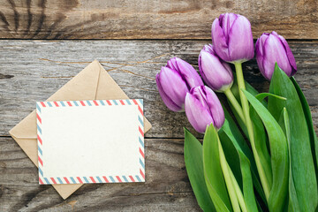 Purple tulip bouquet and blank greeting card on a wooden background, top view, copy space.