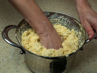 Female hands knead fresh dough for baking bread in an iron pan. Close-up of dough preparation. With one hand, the baker holds the pan and with the other hand kneads wheat dough from white flour