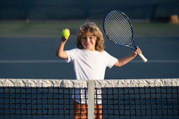 Child playing tennis on outdoor court. Kid with tennis racket and tennis ball playing on tennis court.