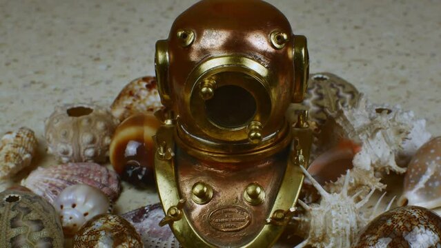 Vintage copper diving helmet with a porthole against the background of many different beautiful sea shells. Flat lay on a marine theme