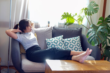 Asian woman lay down and relax on the sofa.She propped her legs up against the table. Put your head...