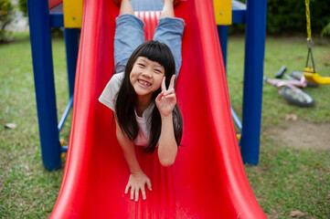 Fototapeta na wymiar Children playing at the playground, happy girl playing slides
